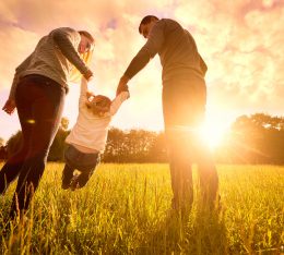 Happy family in the park evening light. The lights of a sun. Mom, dad and baby happy walk at sunset. The concept of a happy family.Parents hold the baby's hands.